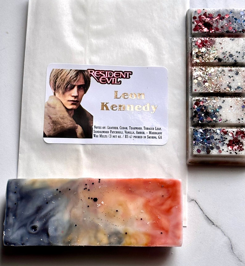 Puede incluir: Un derretimiento de cera con un personaje de la serie de videojuegos Resident Evil, Leon Kennedy. El derretimiento de cera es de color azul claro, blanco y naranja con motas negras. El derretimiento de cera est&aacute; empaquetado en una bolsa de papel blanca con una etiqueta que dice "Resident Evil" y "Leon Kennedy". La etiqueta tambi&eacute;n incluye las notas de aroma: cuero, cedro, teca, hoja de tabaco, s&aacute;ndalo, pachul&iacute;, vainilla, &aacute;mbar, caoba. El derretimiento de cera es de 3 oz netos / 85 ml y se verti&oacute; en Smyrna, GA.