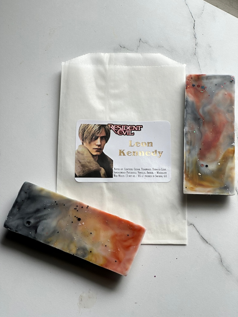 Puede incluir: Dos barras rectangulares de jab&oacute;n hecho a mano con un dise&ntilde;o marmoleado en tonos grises, naranja y marr&oacute;n. El jab&oacute;n est&aacute; etiquetado como "Resident Evil Leon Kennedy" con notas de cuero, cedro, teca, hoja de tabaco, s&aacute;ndalo, pachul&iacute;, vainilla, &aacute;mbar y cal&eacute;ndula. El jab&oacute;n pesa 3 oz y se vierte en el sur de California.