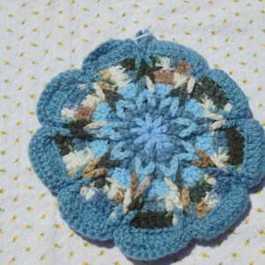 May include: A blue crocheted flower-shaped pot holder with brown, white, and green accents.