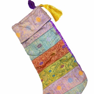 May include: A holiday stocking constructed from horizontal panels of multicolored brocade fabric featuring floral patterns in shades of purple, teal, orange, and gold. The stocking includes a purple hanging loop and a bright yellow tassel.