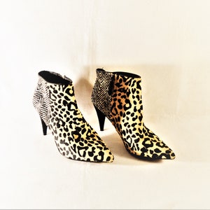 May include: A pair of ankle boots with a pointed toe and stiletto heel. The boots feature a leopard print pattern on the front and a black and white herringbone pattern on the back. The heels are black.