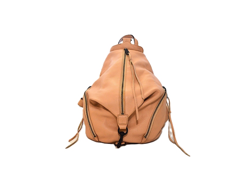May include: A light brown leather backpack with multiple zippered compartments and a top handle. The bag has a rounded shape and features black zippers and hardware. The design includes long zipper pulls and a black clasp.