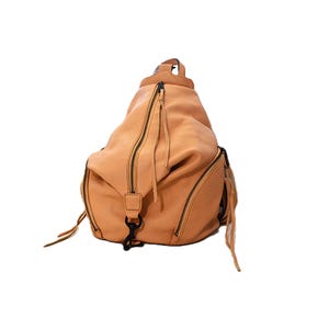 May include: A tan leather backpack with multiple zippered compartments and black hardware. The bag has a rounded shape and features long zipper pulls and a top handle. The leather has a textured appearance.