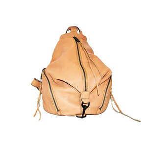 May include: A light tan leather backpack with multiple zippered compartments and black hardware. The bag has a rounded shape with a top handle and adjustable straps. The zippers have long leather pulls.