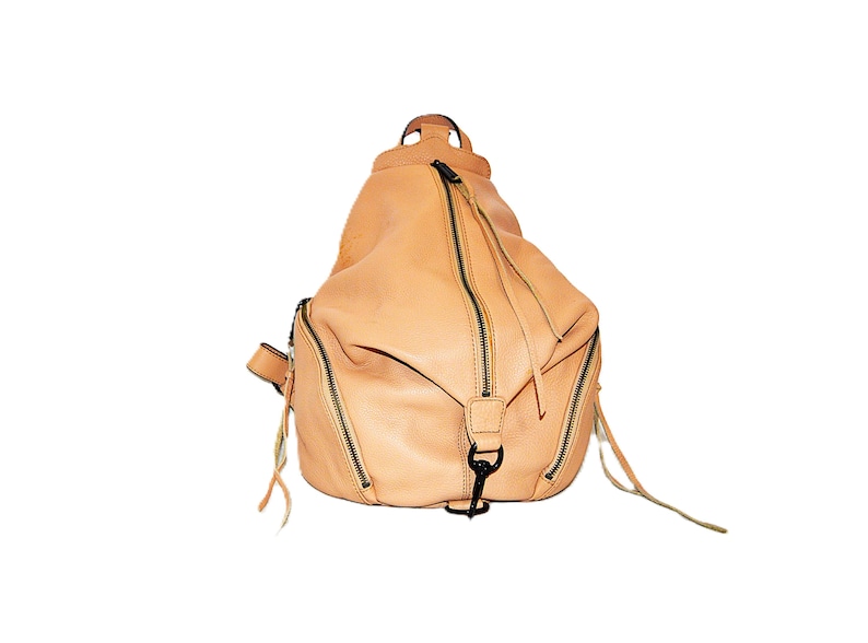 May include: A light tan leather backpack with multiple zippered compartments and black hardware. The bag has a rounded shape with a top handle and adjustable straps. The zippers have long leather pulls.