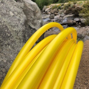 May include: A close-up of a stack of yellow hula hoops. The hoops are made of a flexible plastic material and are designed for exercise and entertainment.