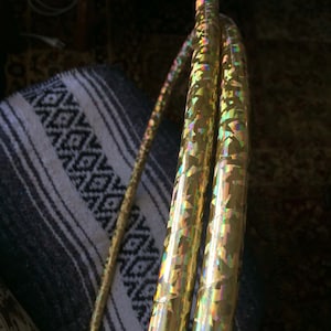 May include: Two gold-coloured hula hoops with a holographic iridescent finish. The hoops are stacked on top of each other.