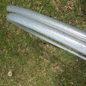 May include: Two silver glitter hula hoops stacked on top of each other. The hoops are lying on a bed of green grass.