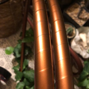 May include: Two copper-coloured metal hoops, each with a textured surface, are stacked on top of each other.