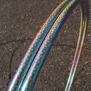 May include: Two iridescent hoops with a geometric pattern. The hoops are made of a shiny, reflective material and have a rainbow-like colour shift.