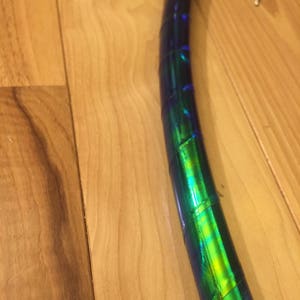 May include: A close-up of a blue and green iridescent hoop, made of plastic tubing. The hoop is wrapped with iridescent tape, creating a shimmering effect.