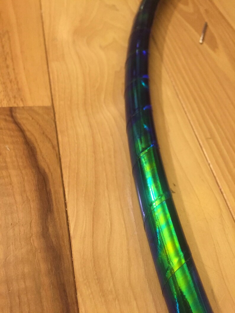 May include: A close-up of a blue and green iridescent hoop, made of plastic tubing. The hoop is wrapped with iridescent tape, creating a shimmering effect.