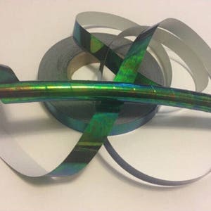 May include: A roll of iridescent green and blue holographic tape. The tape is wrapped around a black spool and is partially unrolled.