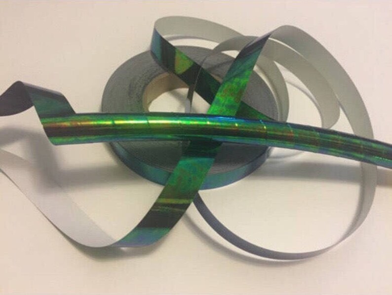May include: A roll of iridescent green and blue holographic tape. The tape is wrapped around a black spool and is partially unrolled.