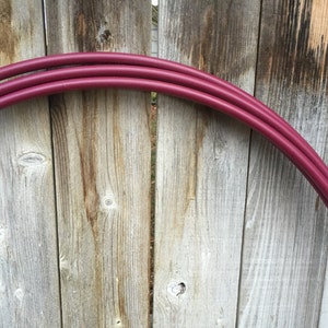 May include: Two burgundy plastic hula hoops stacked on top of each other against a wooden fence.