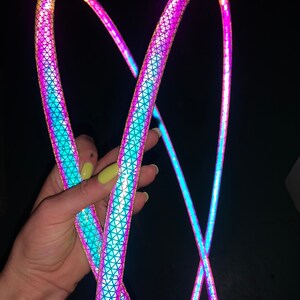 May include: Two iridescent rainbow coloured hula hoops with a geometric pattern. The hoops are held in a person's hand.
