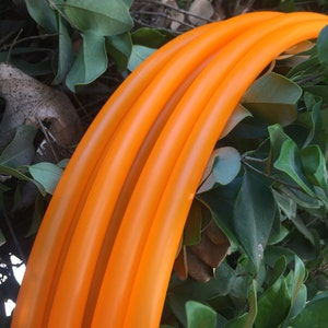 May include: Four orange plastic hula hoops stacked together. The hoops are smooth and shiny.