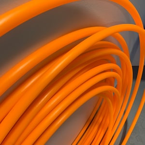 May include: A close-up of a stack of bright orange plastic hula hoops. The hoops are stacked in a circular pattern, creating a visually appealing and colourful image.