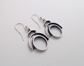 May include: A pair of silver-toned earrings with a unique spiral design. Each earring features a curved, open circle shape with textured detailing and a hook closure. The earrings are displayed against a light background.