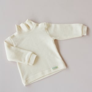 May include: A white long-sleeved turtleneck shirt with a small green label that says "Korleja".