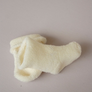 Op de afbeelding: Een paar zachte, witte, pluche sokken. De sokken zijn opgevouwen en gemaakt van een pluche materiaal.
