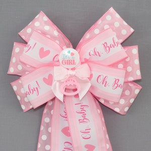 May include: Pink and white polka dot bow with a pink ribbon that says "Oh Baby!" and a pink pacifier charm with a button that says "It's a Girl".