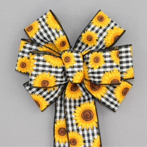 May include: A black and white gingham ribbon bow with a sunflower print. The bow is tied with a long tail and is perfect for decorating a wreath or other craft project.