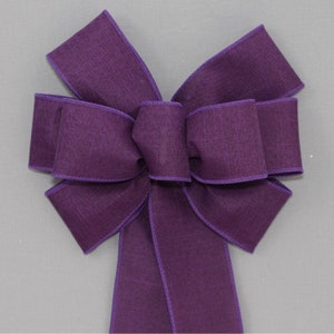 May include: A large purple bow made from wired ribbon. The bow has a center loop and two side loops. The ribbon has a subtle texture and a slight sheen.
