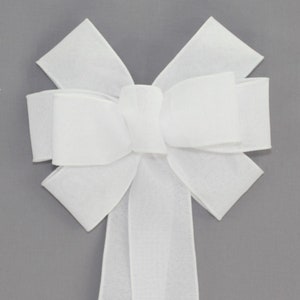 May include: A large white bow made from sheer fabric. The bow has a long tail and is tied in a classic style.