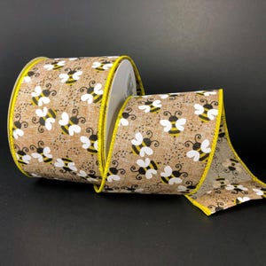 May include: A roll of decorative ribbon featuring a repeating pattern of white and yellow bees on a brown background. The ribbon has a yellow edge and is suitable for crafts and gift wrapping.