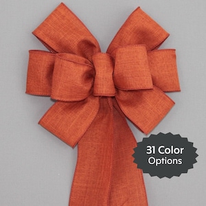 May include: A large, rust-colored bow made from a textured fabric. The bow has a long tail and is tied in a classic, symmetrical style. 31 Color Options.