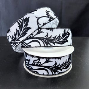 May include: A roll of white ribbon with a black floral design. The ribbon is made of a fabric material and has a black stitched edge. The ribbon is unrolled and displayed on a white spool.