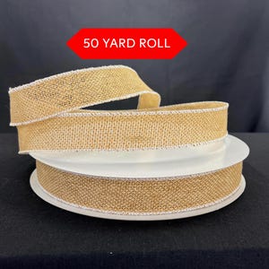 May include: A roll of natural burlap ribbon with a white stitched edge. The ribbon is on a white spool, and the text "50 YARD ROLL" is in a red banner above the ribbon. The ribbon is a light tan color.