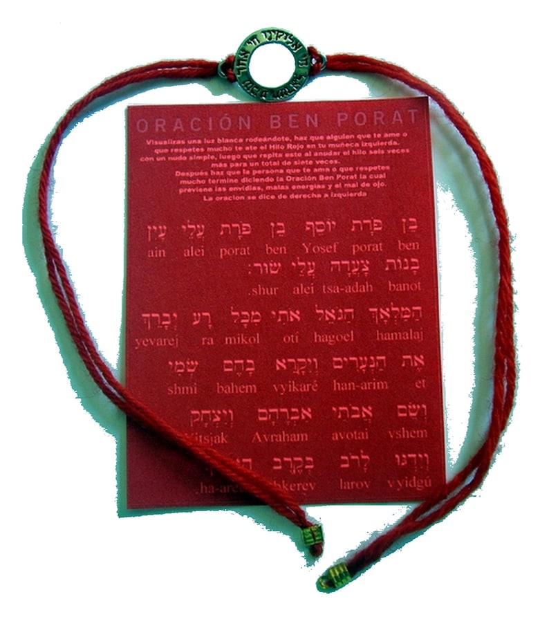 May include: A red string bracelet with a metal charm and a red card with text. The bracelet has a woven design and a metal charm with Hebrew text. The card has text in Hebrew and Spanish.