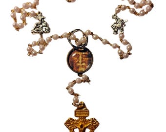 May include: A rosary necklace featuring faux pearl beads and gold-toned metal accents. The necklace includes a crucifix pendant, religious icons, and a circular pendant with a religious image.