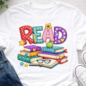 Puede incluir: Camiseta blanca con la palabra "READ" en letras coloridas estilo patchwork. El diseño incluye una pila de libros, una manzana verde y estrellas. El texto "Designs by Susan" está en la parte inferior.