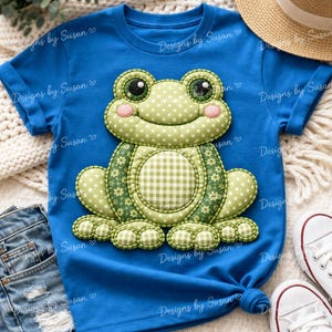 May include: A blue t-shirt featuring a large, appliqued frog design. The frog has a green polka-dot head, floral and gingham patterned body, and pink cheeks. The shirt is styled with denim shorts, a straw hat, and white sneakers.
