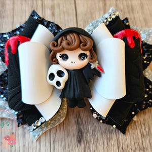May include: A handmade Halloween hair bow featuring a central figure of a cartoon grim reaper holding a skull and a bloody knife. The bow has white, black, and silver glitter accents, with red accents. The bow is a unique accessory.