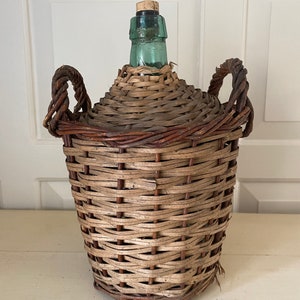 May include: A vintage glass bottle with a woven wicker basket around it. The bottle has a cork stopper and a green glass neck. The basket has two handles.