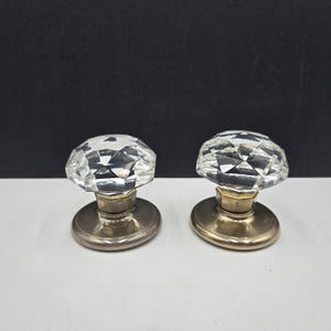 May include: Two vintage crystal door knobs with faceted glass tops and silver-toned metal bases. The knobs have a classic, elegant design, perfect for adding a touch of sophistication to any door or furniture piece.