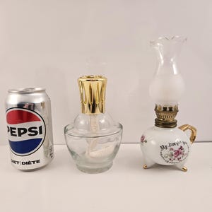May include: Two decorative oil lamps. One is clear glass with a gold top and the other is white porcelain with a gold handle and floral design. The porcelain lamp has the text "My love for you" on the side.