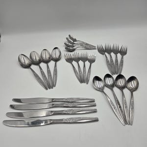 Può includere: Una collezione di posate in acciaio inossidabile, tra cui cucchiai, forchette e coltelli. Le posate hanno un motivo floreale sui manici. Il set comprende varie dimensioni di cucchiai, forchette e coltelli, adatte per una tavola completa.