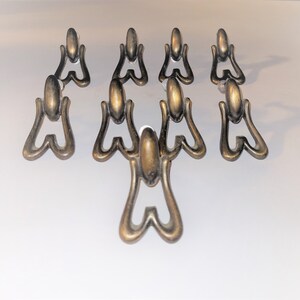 May include: A set of seven antique brass-toned metal drawer pulls arranged in a triangular formation. Each pull features a smooth, rounded top mounting piece connected to a dangling, open-frame, heart-shaped handle with a weathered metallic finish.