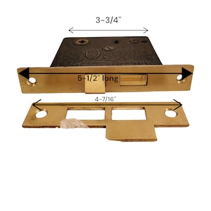 Może przedstawiać: Zamek do drzwi z mosiądzu z płytką czołową o długości 14 cm i płytką przednią o długości 11,1 cm. Zamek ma wysokość 9,5 cm.