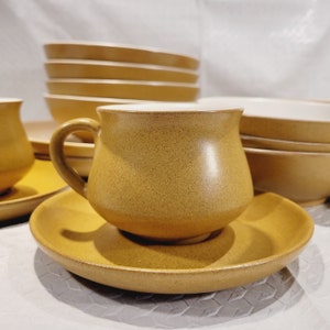 May include: A set of brown ceramic bowls and a matching cup and saucer. The bowls are stacked on top of each other, and the cup and saucer are in front of them.
