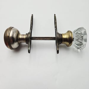 Puede incluir: Juego de manijas de puerta antiguas con un pomo de vidrio transparente facetado y un acabado de latón y metal deslustrado. El juego incluye dos pomos, una varilla de conexión y dos placas traseras. Diseño vintage para proyectos de restauración.