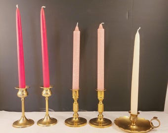 Può includere: Cinque portacandele in ottone con candele. Due portacandele hanno candele rosse, due hanno candele rosa e uno ha una candela bianca.
