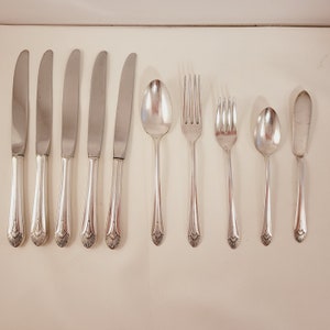 Peut inclure: Un ensemble de couverts, comprenant des couteaux, des fourchettes et des cuillères, tous avec des manches ornés. Les couverts sont en argent et ont une finition polie.