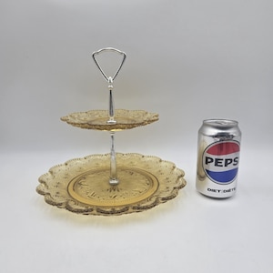 Könnte beinhalten: Ein zweistufiges, bernsteinfarbenes Serviertablett mit einem silbernen Griff. Das Tablett hat einen dekorativen, gewellten Rand und ein detailliertes Blumenmuster. Eine Diet Pepsi-Dose befindet sich neben dem Tablett.