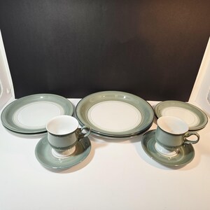 May include: A set of vintage stoneware dishes in a soft green and white color scheme. The set includes plates, saucers, and teacups. The plates and saucers have a white center with a green border. The teacups are green with white interiors.